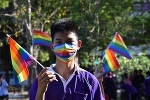 porträtt asiatisk ung pojke innehar regnbåge flagga, HBTQ symbol, i händer medan sammanfogning hans HBTQ aktivitet på skola, begrepp för HBTQ gemenskap firande i stolthet månad, juni, 2023, runt om de värld. foto