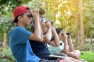 tre sydöst asiatisk Pojkar är använder sig av kikare till observera fåglar i tropisk skog, aning för inlärning varelser och vilda djur och växter djur utanför de klassrum. foto