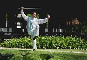 ung man praktiserande traditionell tai chi svärd, tai ji i de parkera för friska, traditionell kinesisk krigisk konst begrepp på naturlig bakgrund . foto