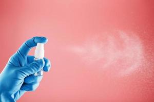 en blåhandskar hand innehar en desinfektionsmedel på en rosa bakgrund. antiseptisk behandling av händer från bakterie desinfektionsmedel. foto