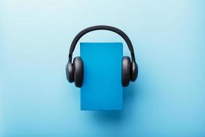 hörlurar är bärs på en bok i en blå hårt omslag på en blå bakgrund, topp se. foto