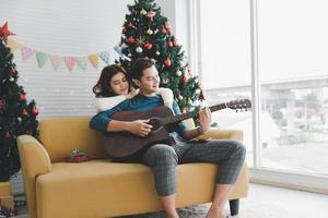 en man spelar gitarr till kvinna älskare under firar jul Semester tillsammans i levande rum med jul träd prydnad dekoration foto