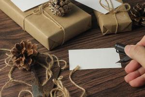 manlig händer omslag ny år gåvor och skrivning kort på en brun trä- tabell. foto