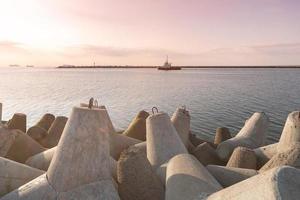 fartyg-bogserbåt går i öppet hav för att bogsera lastfartyg till hamn. vacker solnedgång över piren. tetrapod vågbrytare i hamnen. foto