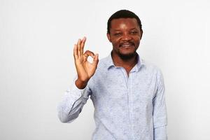 Lycklig afrikansk amerikan svart man med ok gest i tillfällig ljus skjorta isolerat på vit bakgrund foto