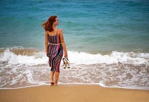 Lycklig ung boho kvinna gående och har roligt i de hav vågor på en solig värma dag på en tropisk ö. foto