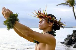 manlig hula dansare utför på de strand med uttrycksfull bön- hand rörelser. foto