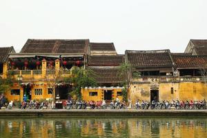 hoi en, vietnam - februari 12, 2018. de vägbank av tor bon flod med gul byggnader och traditionell trä- båtar. de historisk gammal stad av hoi ett är unesco värld arv webbplats. foto
