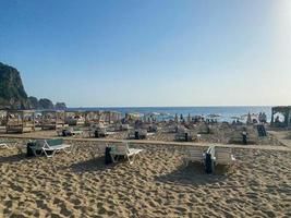 massor av Sol solstolar på en sandig strand med en berg och hav i en värma tropisk orientalisk sydlig Land tillflykt foto