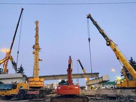 konstruktion av en bruten bro på en upptagen väg. konstruktion Utrustning på en sektion av de väg reser sig ett viadukt, en kran bär tung betong block foto