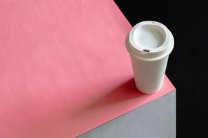 en vit återvinna tumlare av kaffe sätta på rosa, grå och svart Färg papper för värld miljö begrepp. foto