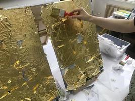 de konstnärens hand målarfärger med en borsta använder sig av guld glittrande ljus gul metallisk guld blad för konstnärlig syften och kreativitet på duk. de bakgrund foto