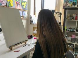 kvinna konstnär med lång hår drar en bild i de konstnärens kreativ konst verkstad med målarfärger och borstar på de tabell av de konst skola foto