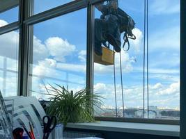 en manlig fönster bricka arbetstagare, industriell klättrare hänger på en lång byggnad, skyskrapa och tvättar stor glas fönster för renlighet hög ovan en stor stad i ett kontor företag byggnad foto