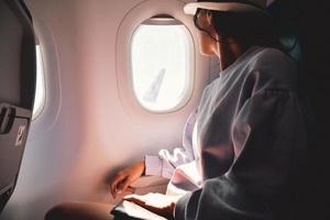 kvinna utseende ut de fönster av ett flygande flygplan. ung caucasian Lycklig passagerare är reser förbi plan, tittar på de himmel från ovan och håll pass foto
