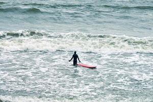 manlig surfare i baddräkt i havet med röd surfbräda foto
