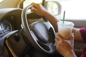 närbild hand håll kopp av iced kaffe till dryck i bil. begrepp, baverge för uppfriskande eller portion till vaken från sovande under körning den där kan orsak bil olycka. foto