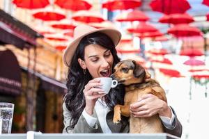 ung kvinna med henne hund i sällskapsdjur vänlig cafeteria. flicka dricka coffe på lokal- kaffe affär med henne sällskapsdjur hund foto