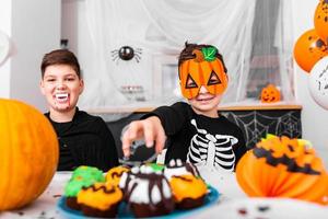 Lycklig halloween attraktiv ung pojke med hans bror är framställning för halloween fest. bröder i kostymer är har roligt med pumpor och cupcakes. foto