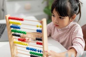en ung söt asiatisk tjej använder kulramen med färgade pärlor för att lära sig att räkna hemma foto