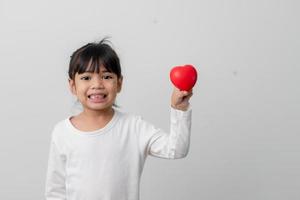 porträtt av asiatisk liten flicka barn innehav röd hjärta tecken på vit bakgrund foto