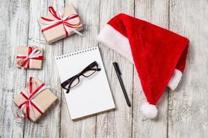 jul och företag objekt med kopia Plats santa keps anteckningsblock penna glasögon och dekorerad gåva lådor foto