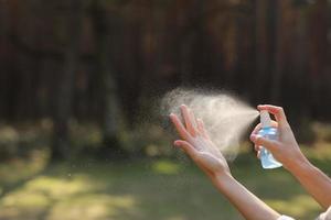 kvinnans hand trycker alkoholspray i naturen för att rengöra hennes hand. alkoholspray är mycket viktigt i det dagliga livet. myggmedel eller antiseptisk foto