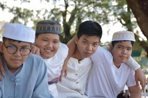 ung asiatisk muslim Pojkar är spelar med deras händer Bakom varje Övrig förbi Sammanträde i en rad lyckligt under en träd i de skola parkera, mjuk och selektiv fokus. foto