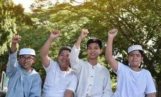 ung asiatisk muslim Pojkar är höjning deras rätt händer till visa deras seger och Framgång lyckligt under en träd i de skola parkera, mjuk och selektiv fokus. foto