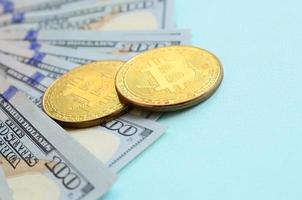gyllene bitcoins och hundra dollar räkningar lögner på ljus blå bakgrund foto