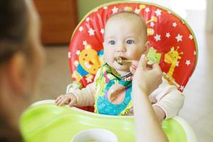 mamma matar rolig bebis från en sked . barn äter i en barnstol foto