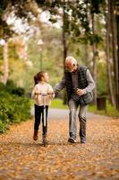 senior man undervisning hans barnbarn på vilket sätt till rida sparka skoter i parkera foto