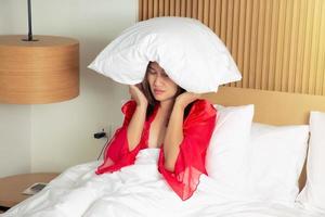 kvinna i en satin röd nattlinne liggande på säng och stängning henne huvud med de kudde på natt. asiatisk kvinna lidande från sömnlöshet eller depression. foto