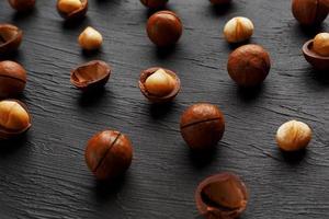 renades och skal upprepningar macadamia nötter på svart textural sten bakgrund. friska äter begrepp foto