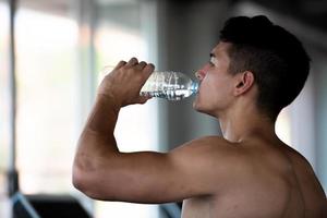 ung caucasian friska sporter man dricka vatten i de sport Gym efter träna på löpband. foto