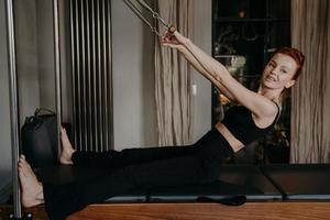 ung vacker kvinna med leende gör övningar på pilates reformer foto