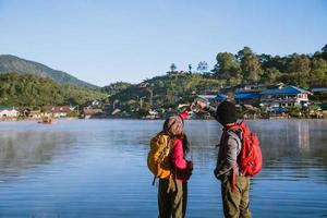 asiatisk kvinna och asiatisk man som backpackade stående nära sjön, hon log, glad och njöt av dimmans naturliga skönhet. foto