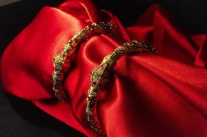 en par av gyllene armband placerad på en röd sammet trasa. de guld smycke glittrar med rik arbete traditionell motiv och stor mönster. foto