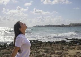 avslappnad kvinna andas färsk luft på de stenar förbi de medelhavs hav foto