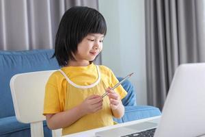 liten asiatisk flicka studerande studie uppkopplad använder sig av bärbar dator dator på Hem foto