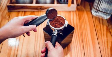 Barista häller kaffe böna rosten pulver jord kaffe häller in i en portafilter med en Barista hand på de kaffe affär foto