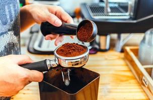 Barista häller kaffe böna rosten pulver jord kaffe häller in i en portafilter med en Barista hand på de kaffe affär foto