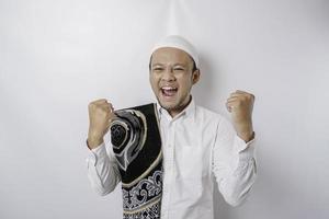 en Lycklig ung asiatisk muslim man med en bön matta på hans axel som visar en framgångsrik uttryck isolerat förbi vit bakgrund foto