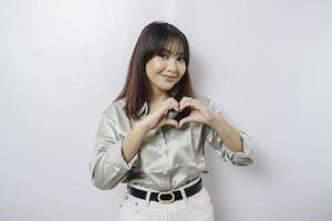 ett attraktiv ung asiatisk kvinna bär en salvia grön skjorta känner Lycklig och en romantisk former hjärta gest uttrycker anbud känslor foto