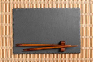 tömma rektangulär svart skiffer tallrik med ätpinnar för sushi på trä- bakgrund. topp se med kopia Plats foto