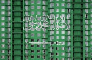 saudi arabien flagga avbildad i måla färger på flera våningar bosatt byggnad under konstruktion. texturerad baner på tegel vägg bakgrund foto