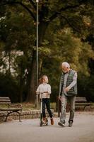 senior man undervisning hans barnbarn på vilket sätt till rida sparka skoter i parkera foto