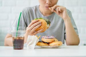 nöjd asiatisk kvinna äter friterad kyckling burger och franska pommes frites. ohälsosam äter begrepp. foto