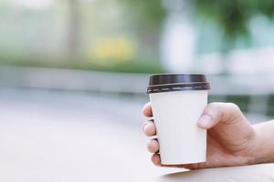 hand som håller papperskopp med take away dricker kaffe på naturligt morgonsolljus. plats för din logotyp. lämna utrymme för att skriva text. foto