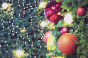 närbild av grannlåt färgglad sort hängande från en dekorerad julgran på suddiga ljus med dekorerad träd, gnistrande och bokeh bakgrund. kopiera utrymme för din text. julgransdekoration foto